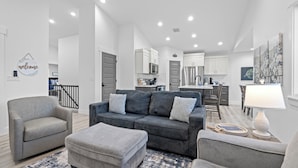 A modern living room with a grey sofa, two armchairs, and a matching ottoman. A dining area with a table and chairs is visible in the background. - Beautiful & Spacious 3BR Retreat | Clean, Quiet, Sleeps 8 (Idaho Falls)