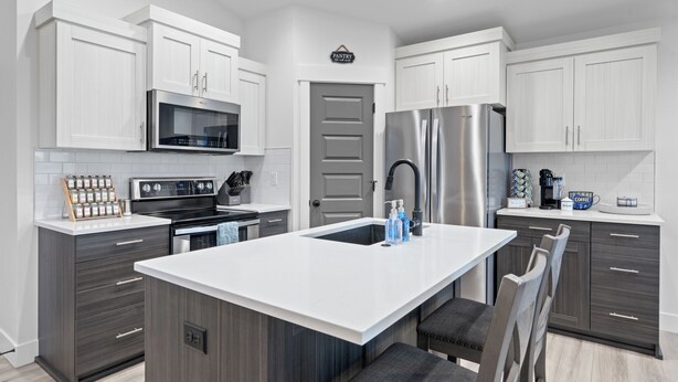A modern kitchen with white cabinets, a stainless steel refrigerator, a built-in oven, and a large island with bar stools. - Beautiful & Spacious 3BR Retreat | Clean, Quiet, Sleeps 8 (Idaho Falls)