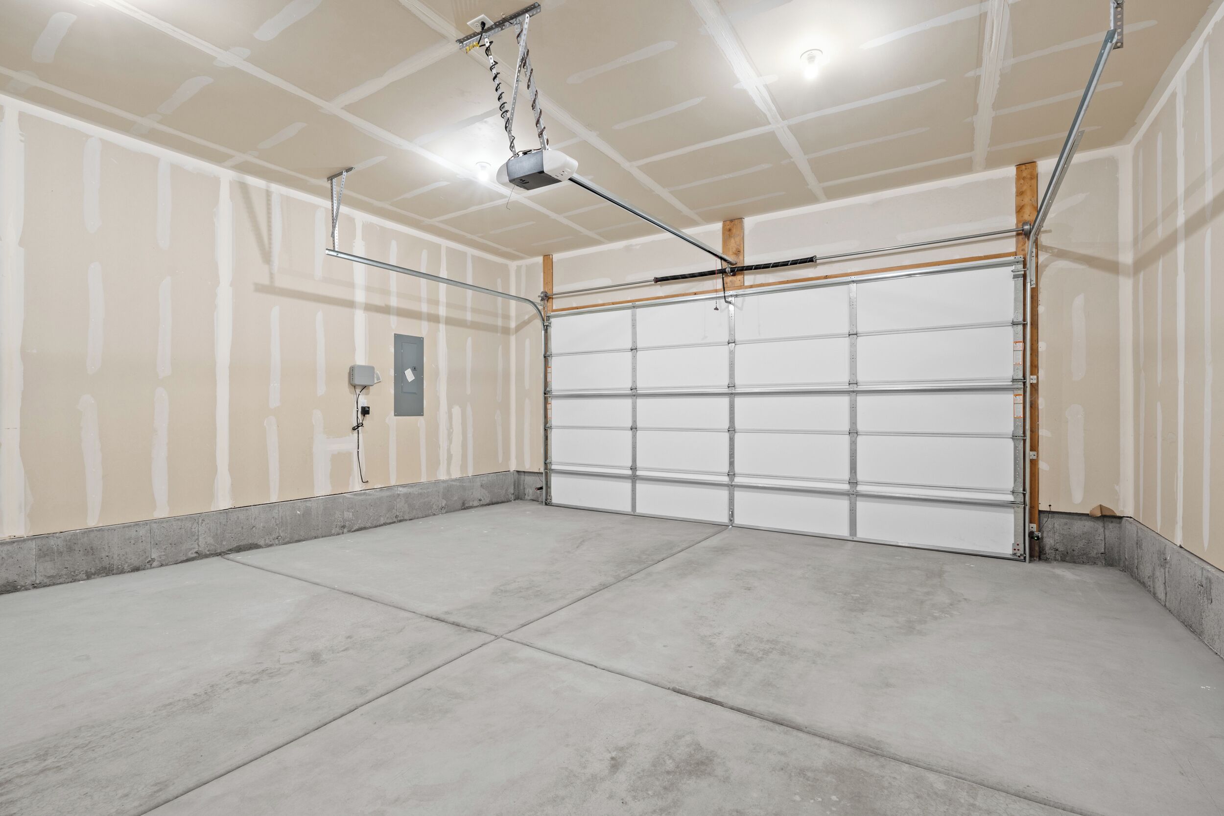 En garage med beton gulv, lukket garageport og projektor monteret i loftet.