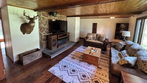 Een gezellige woonkamer met een stenen openhaard, houten plafond en een opgehangen hertenkop.