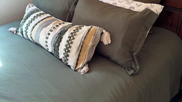 Een bed met groen beddengoed en twee kussens, waarvan één met een patroon en één effen.