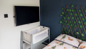 Ein Schlafzimmer mit einem Bett, einem an der Wand montierten Fernseher und einem Babybett.
