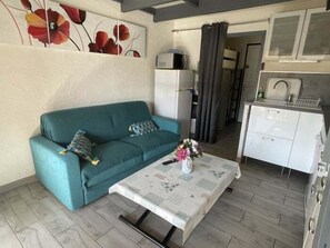A living room with a sofa, a coffee table with flowers, a white cabinet, and a kitchen area with a sink and cabinets.