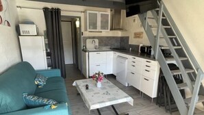 Een knus woongedeelte met een bank, een klein tafeltje met een vaas, een kitchenette en een trap.