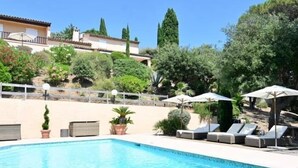 A swimming pool with lounge chairs and umbrellas, surrounded by greenery and a building in the background. - Villa Provençale **** | 5 bedrooms | swimming pool (Sainte-Maxime)