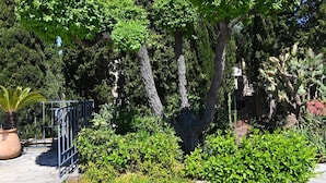 A garden with various plants and trees, a metal fence, and a stone pathway. - Villa *** 120m² | sea view | 800m from the beaches (Les Issambres)