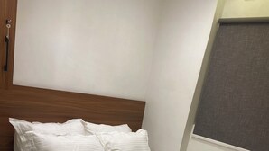 Ein ordentlich bezogenes Bett mit weißer Bettwäsche und gerollten Handtüchern, ein hölzerner Kopfteil und ein Fenster mit Jalousie.