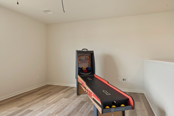 A room with a shuffleboard table, a basketball hoop, and a small basketball court.