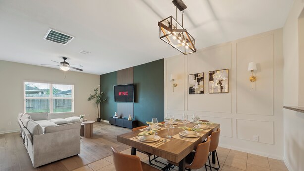 Un salon moderne avec un canapé, une table à manger pour six personnes et un téléviseur à écran plat fixé au mur.