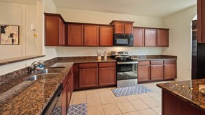 Une cuisine dotée de plans de travail en granit, d’appareils électroménagers en acier inoxydable et d’armoires en bois.