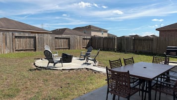 Een achtertuin met een betonnen terras, tuinmeubilair, een barbecue en een houten schutting.