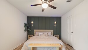 Une chambre à coucher comprenant un lit, des tables de chevet, un ventilateur de plafond et un banc.
