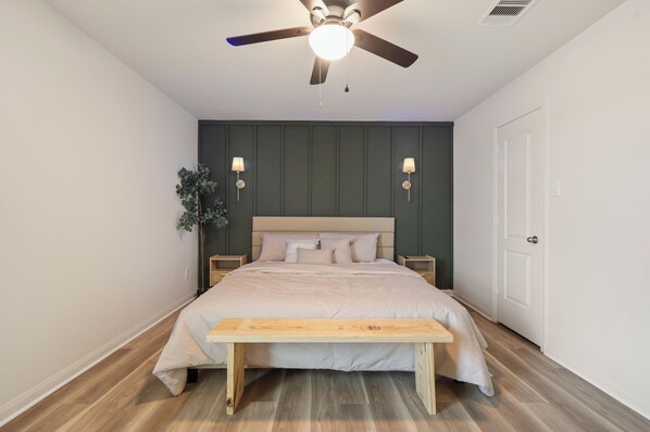 Une chambre à coucher comprenant un lit, des tables de chevet, un ventilateur de plafond et un banc.