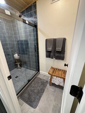 A bathroom with a shower, a bench, and towels on the wall. - Hunter Mountain Hideaway, Cozy Mountain Escape. (Hunter)