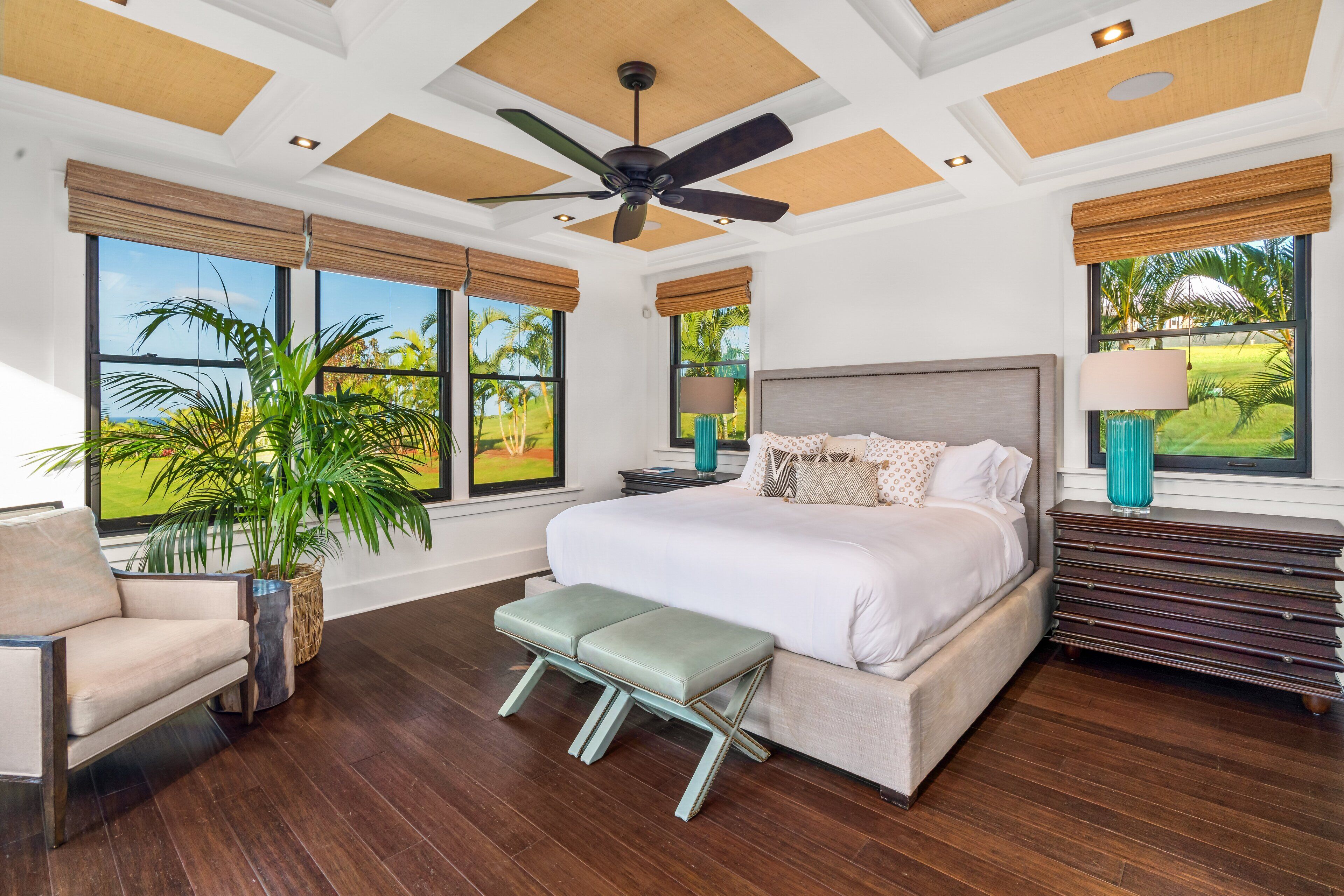 Un dormitorio moderno con una cama grande, un ventilador de techo y ventanas amplias con vistas a palmeras.