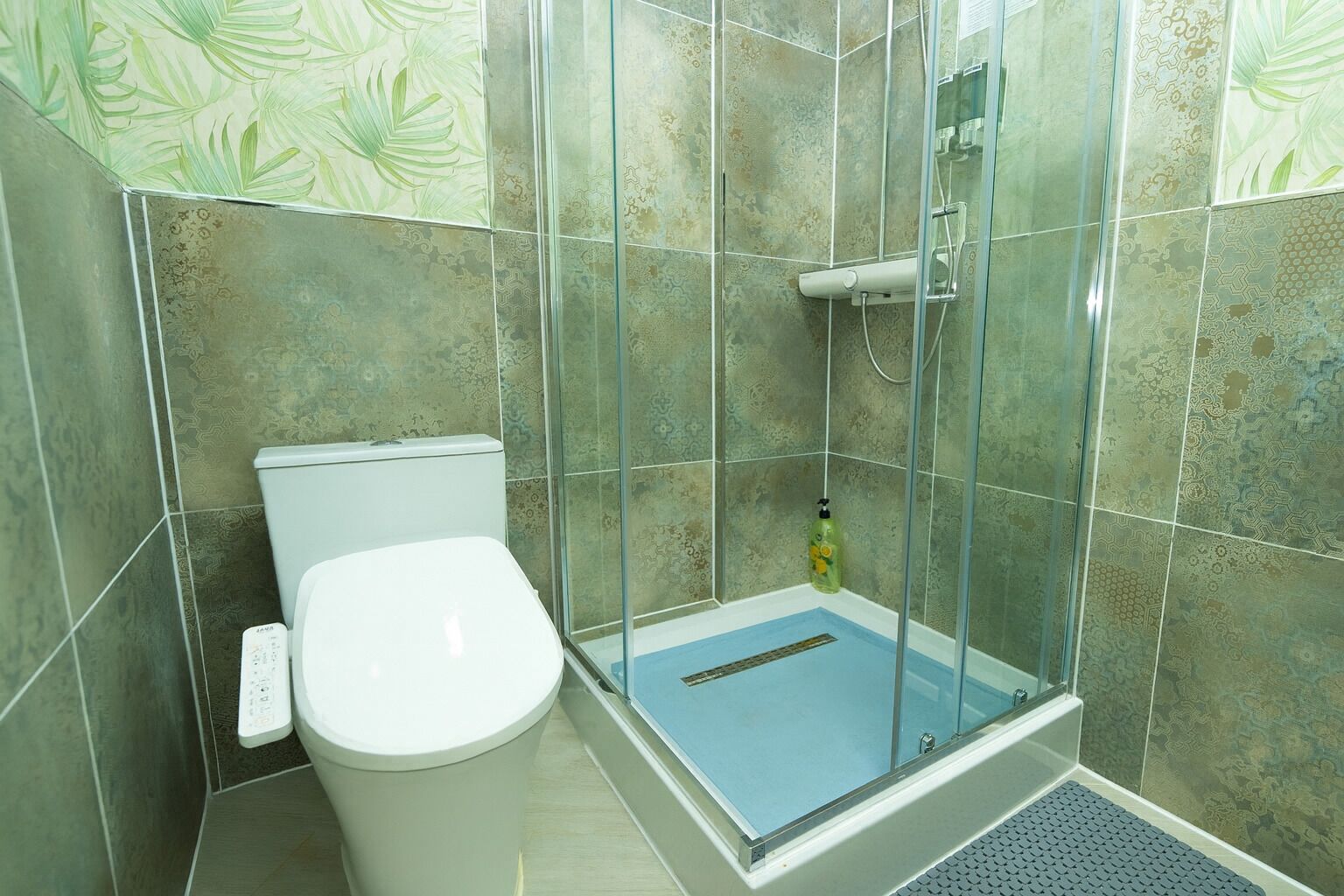 Un box de ducha con puerta de vidrio, un inodoro y baldosas estampadas.