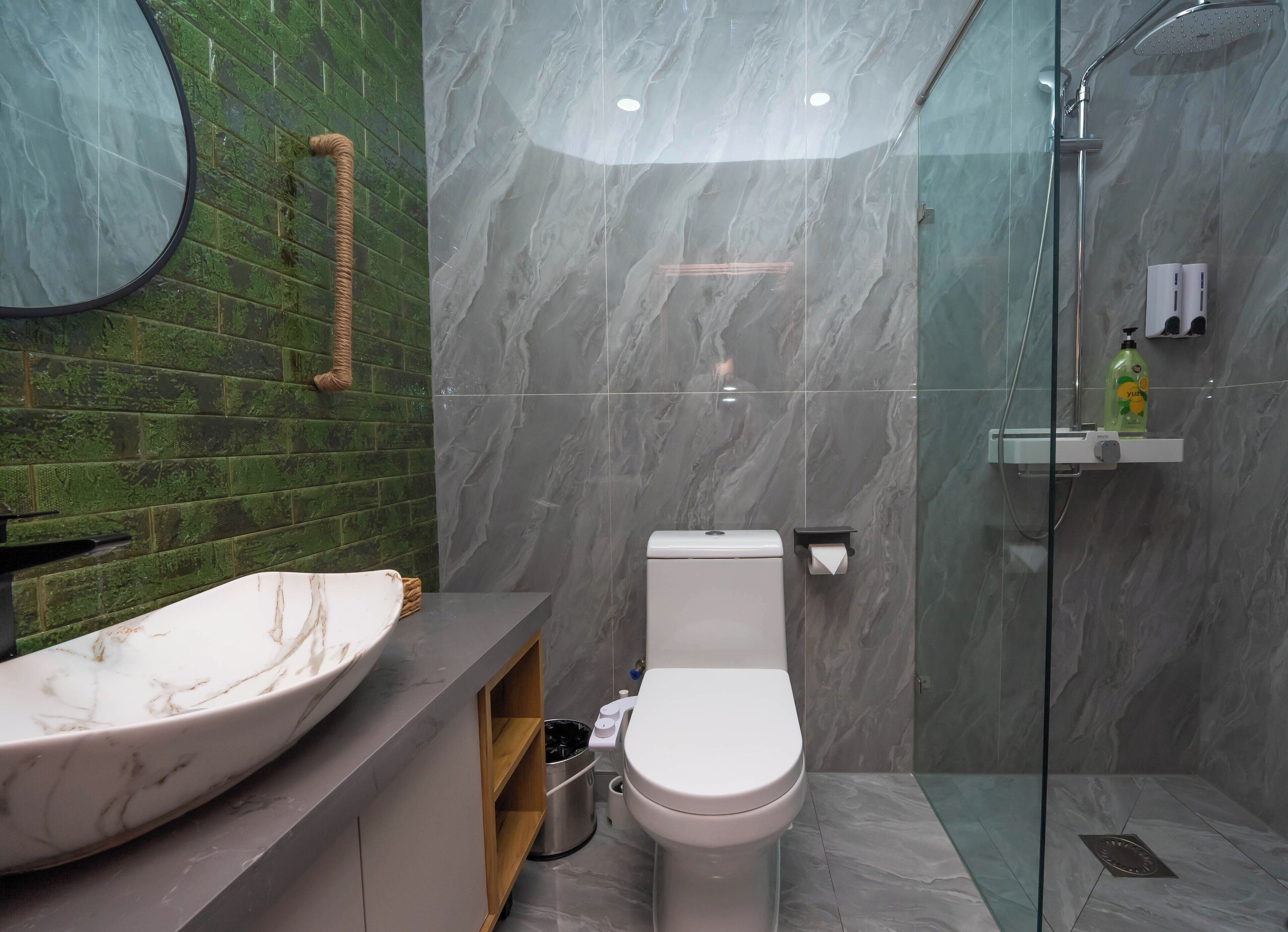 Een badkamer met een marmeren wastafel, toilet, een douchecabine met glazen wanden en een wand betegeld met groene tegels.