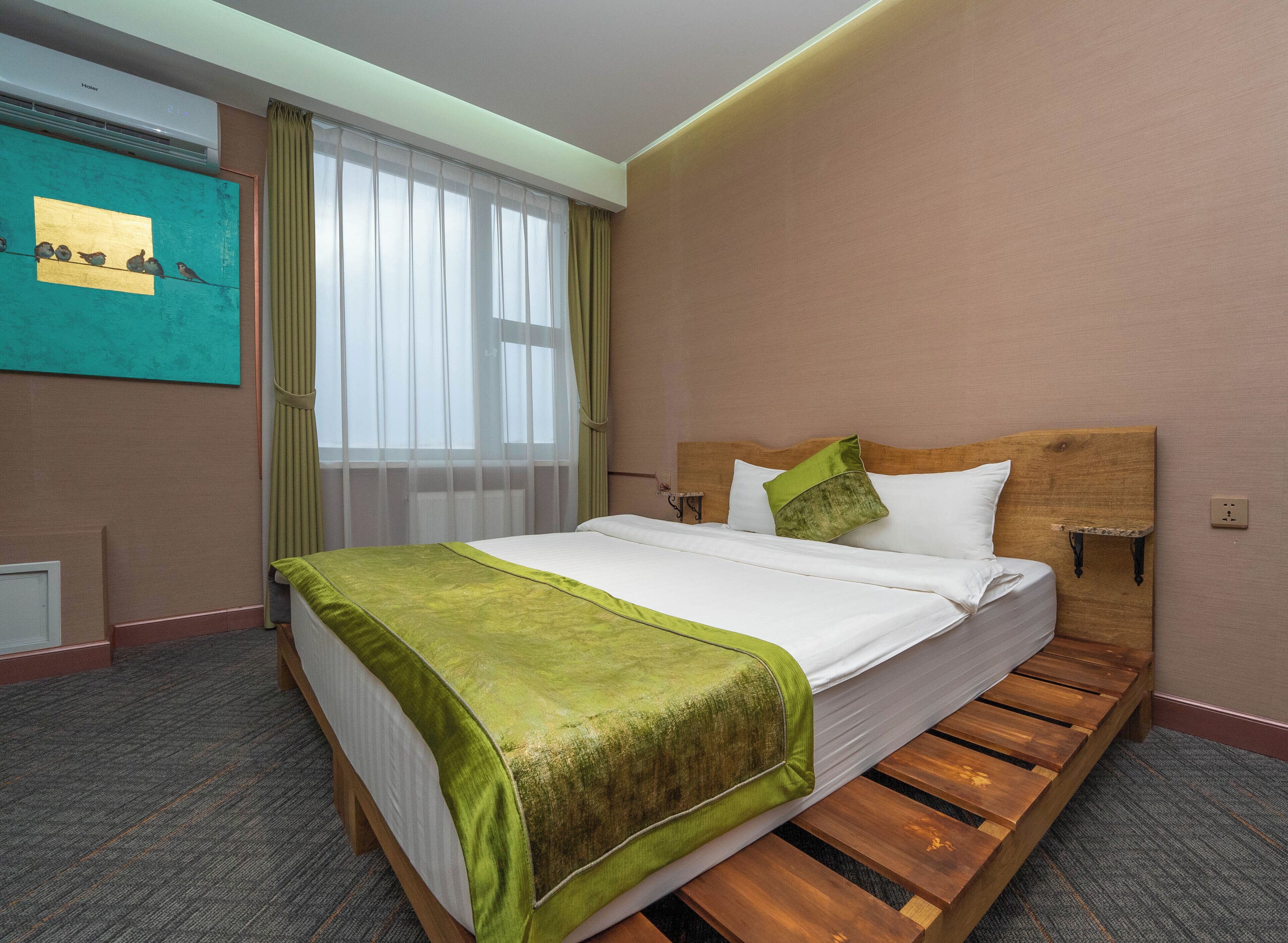 Una habitación de hotel con una cama, un cuadro en la pared, una ventana con cortinas y un cabecero de madera.