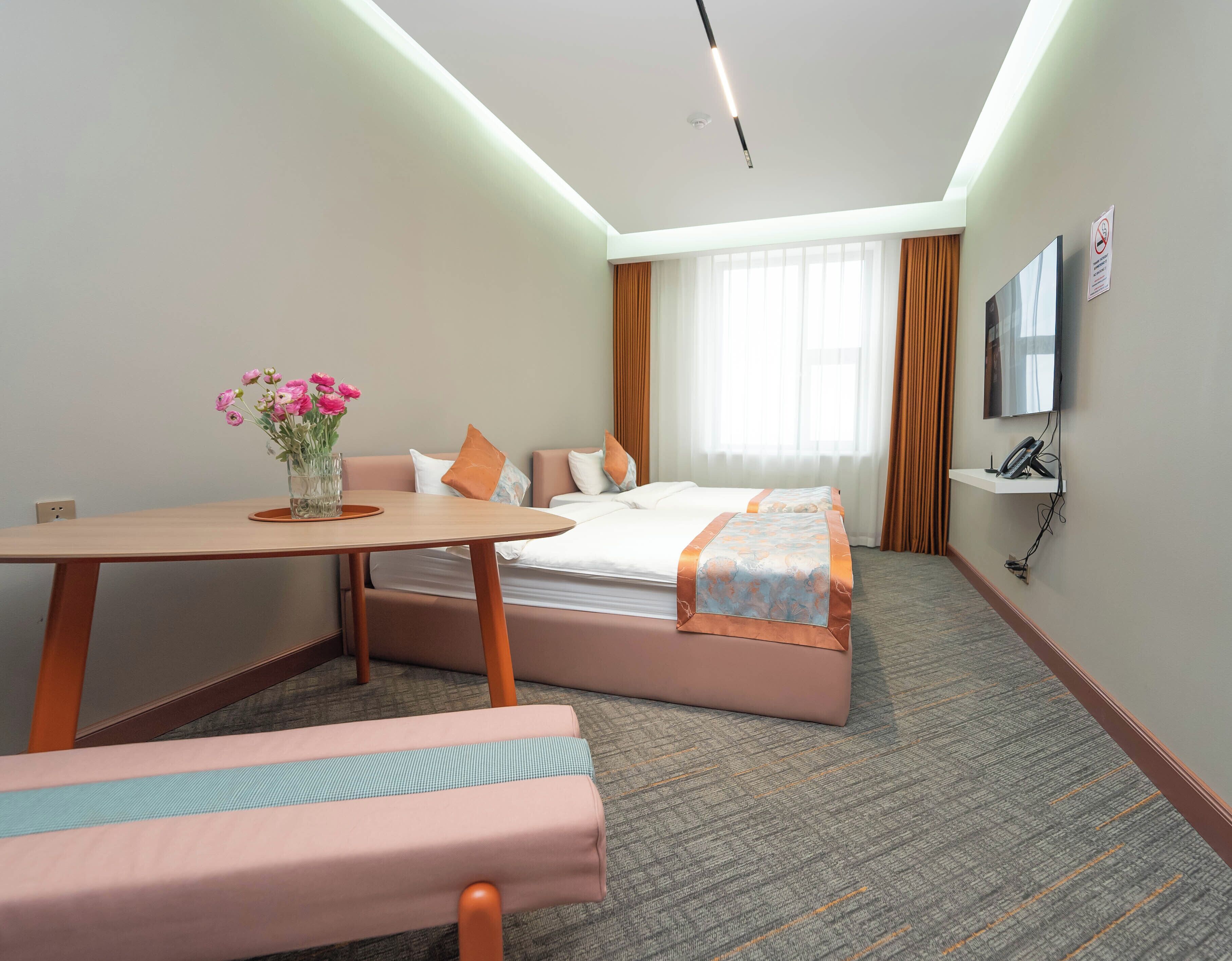 A hotel room with a bed, a desk, a chair, a TV, and a window with curtains.