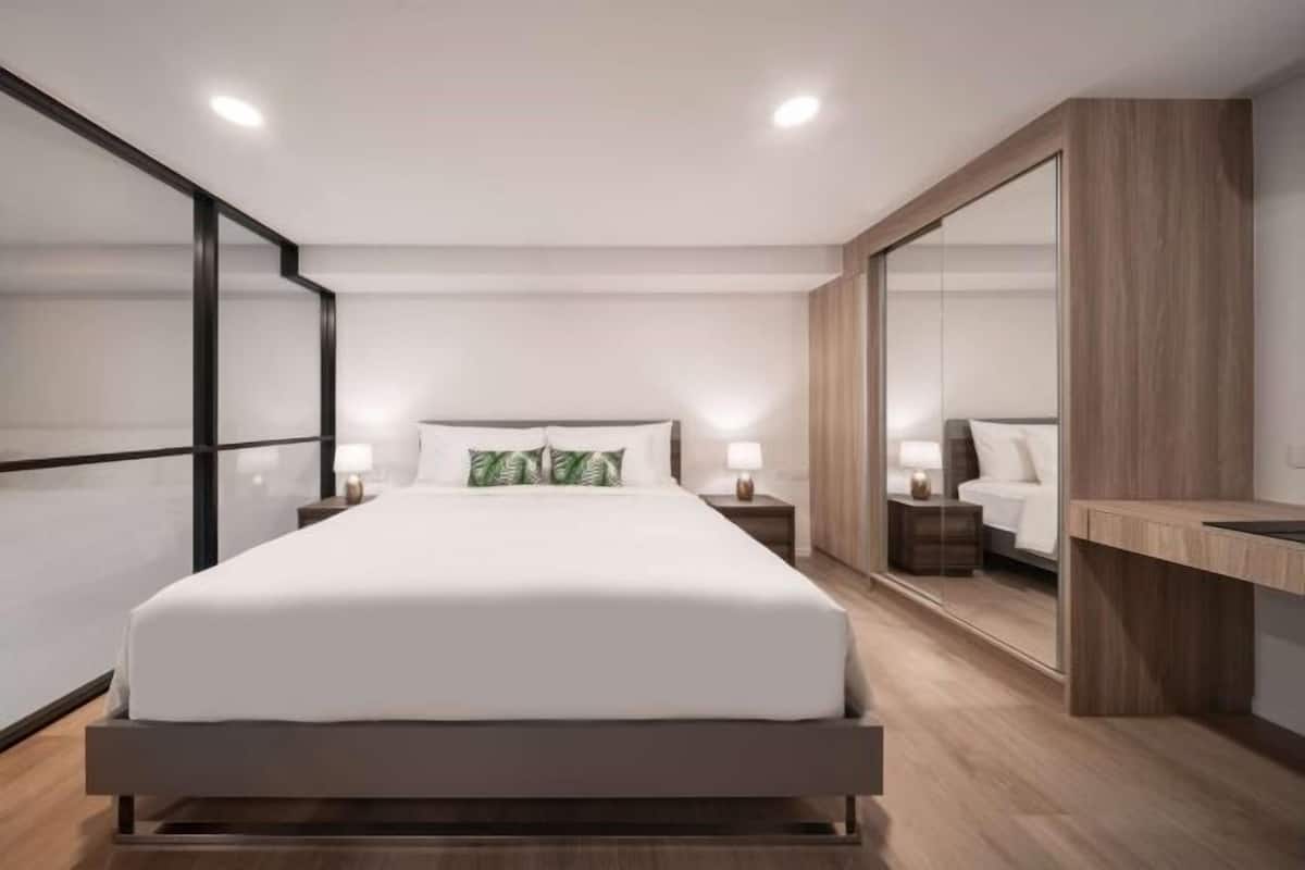 A modern bedroom with a large bed, bedside tables, a mirror, and a wooden desk.