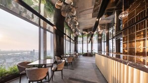 A modern interior with a long counter and seating area, large windows offering a city view, and hanging pendant lights. - Ramada by Wyndham Bangkok Sukhumvit 87 (Bangkok)