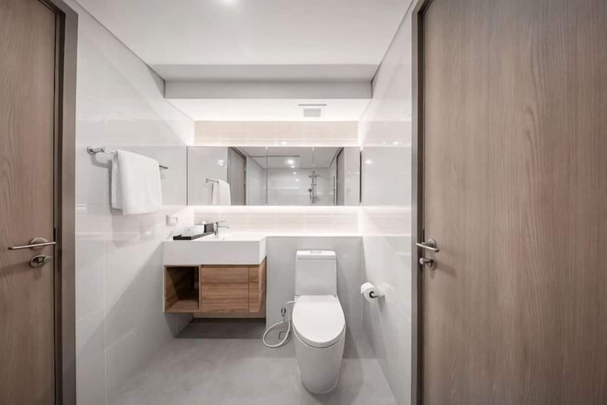 A modern bathroom with a toilet, sink, mirror, and wooden cabinet.