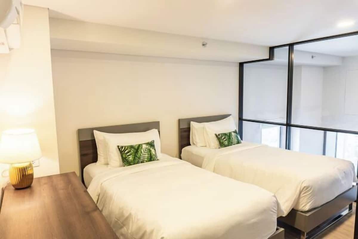 A hotel room with two beds, a nightstand, a lamp, and a large window.