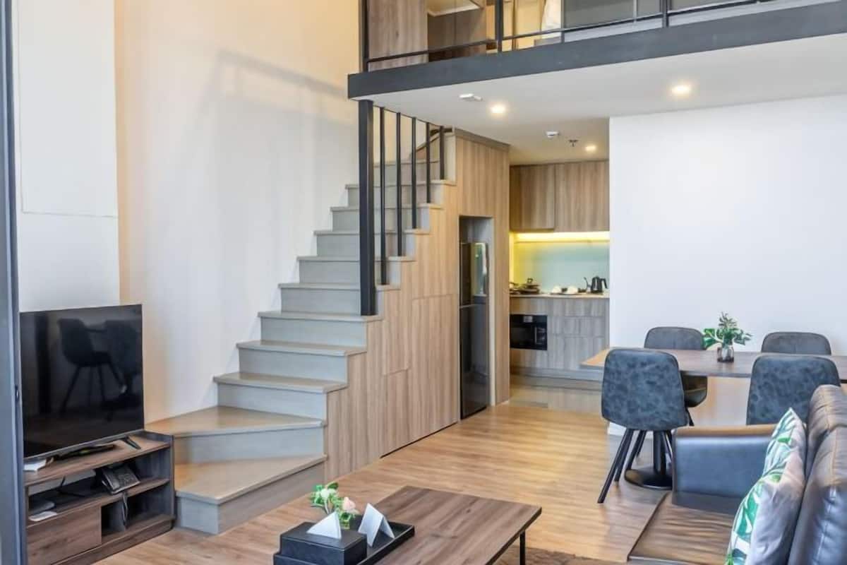 A modern living space with a staircase, a dining area, and a kitchen in the background.