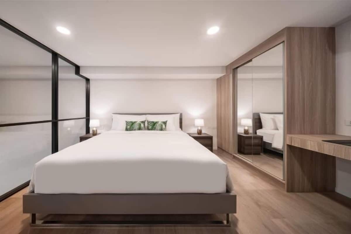 A modern bedroom with a large bed, bedside tables, a mirror, and a wooden bench.