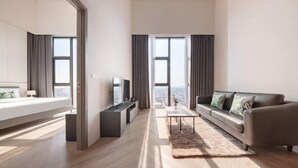 A modern hotel room with a bed, a TV, a sofa, a coffee table, and large windows. - Ramada by Wyndham Bangkok Sukhumvit 87 (Bangkok)