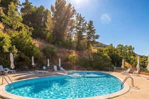 Une piscine entourĂ©e dâarbres et de collines, avec des chaises longues et des parasols.