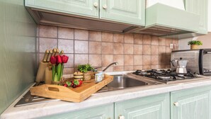 Una cocina con armarios verdes, un salpicadero de azulejos, una tabla de cortar de madera con verduras y una estufa a gas.