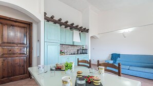 Comedor con mesa lista para dos personas, cocina al fondo y sofá azul.