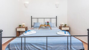 Habitación de hotel ordenada con cama, mesitas de noche, una mesita de bandeja y una planta pequeña.