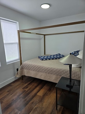 Une chambre à coucher avec un lit à baldaquin, une table de chevet avec une lampe et une fenêtre avec des stores.
