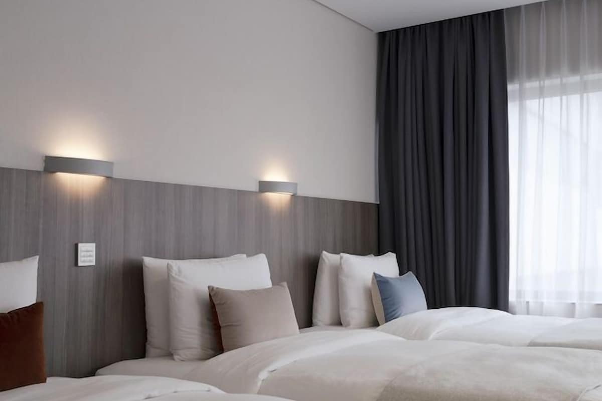 A hotel room with two beds, a grey headboard, and a large window with curtains.