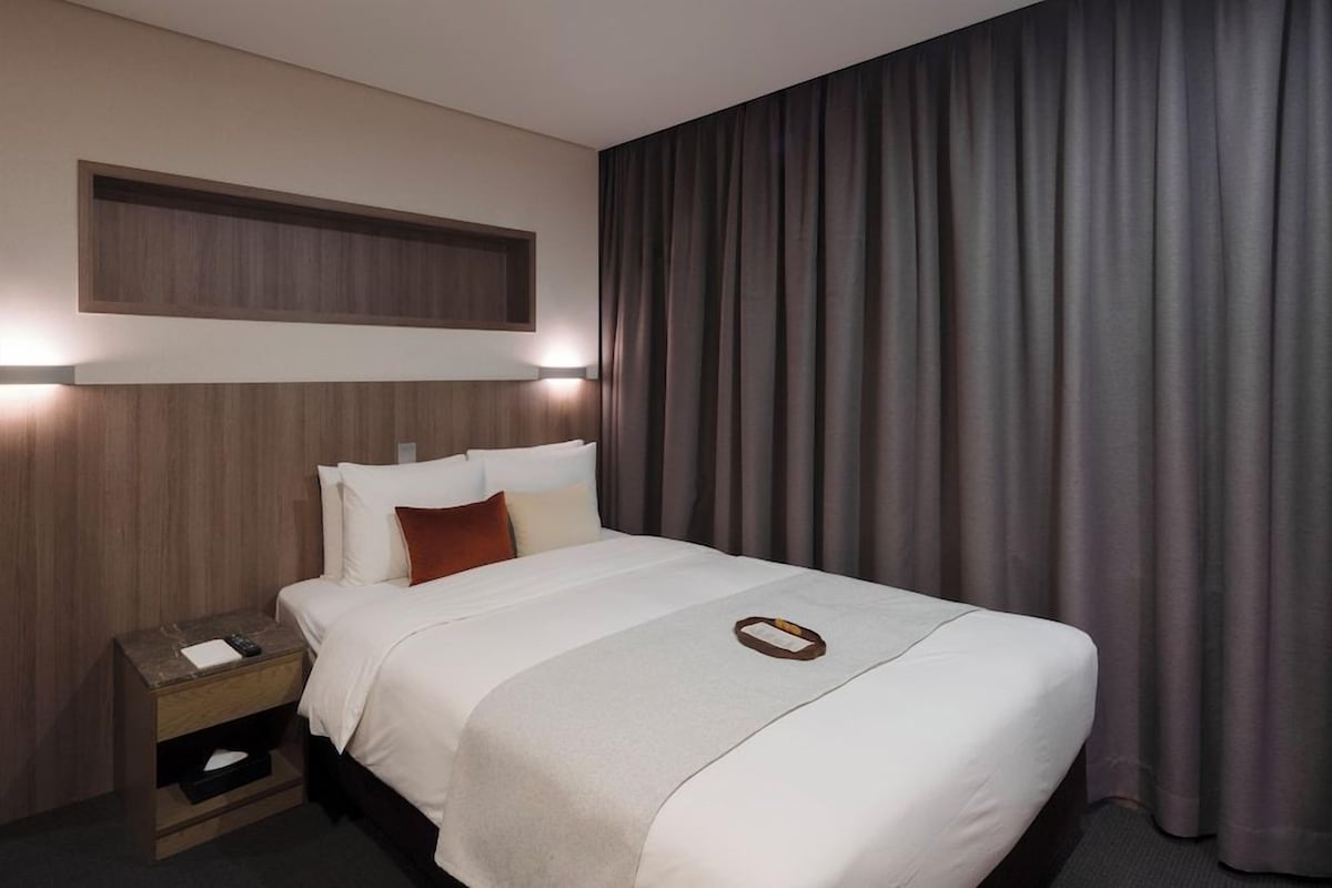 A hotel room with a bed, nightstand, and a large window with curtains.