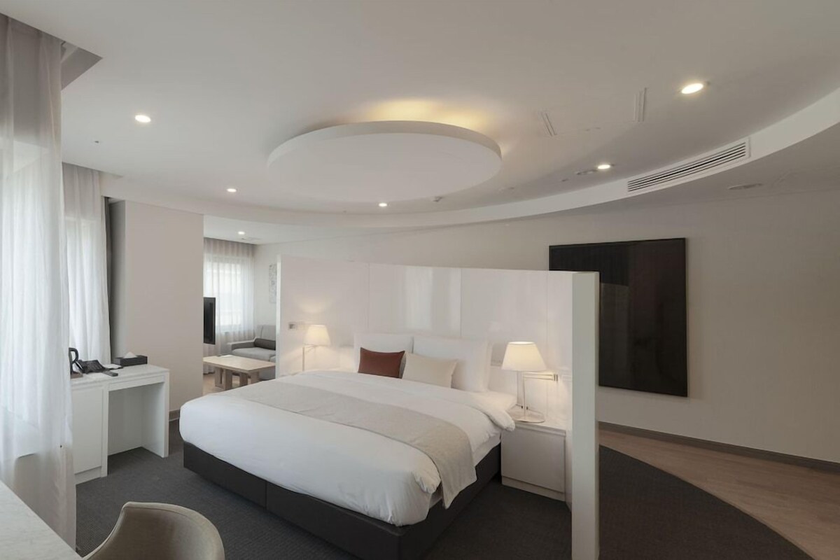 A modern hotel room with a large bed, bedside tables, a desk, and a chair.