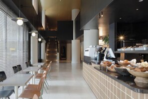 A modern cafe with a long counter, seating area, and a staircase in the background. - Amid Hotel Seoul (Seoul)