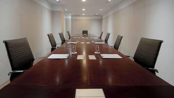 Uma sala de conferências com uma mesa comprida, cadeiras e garrafas de água.