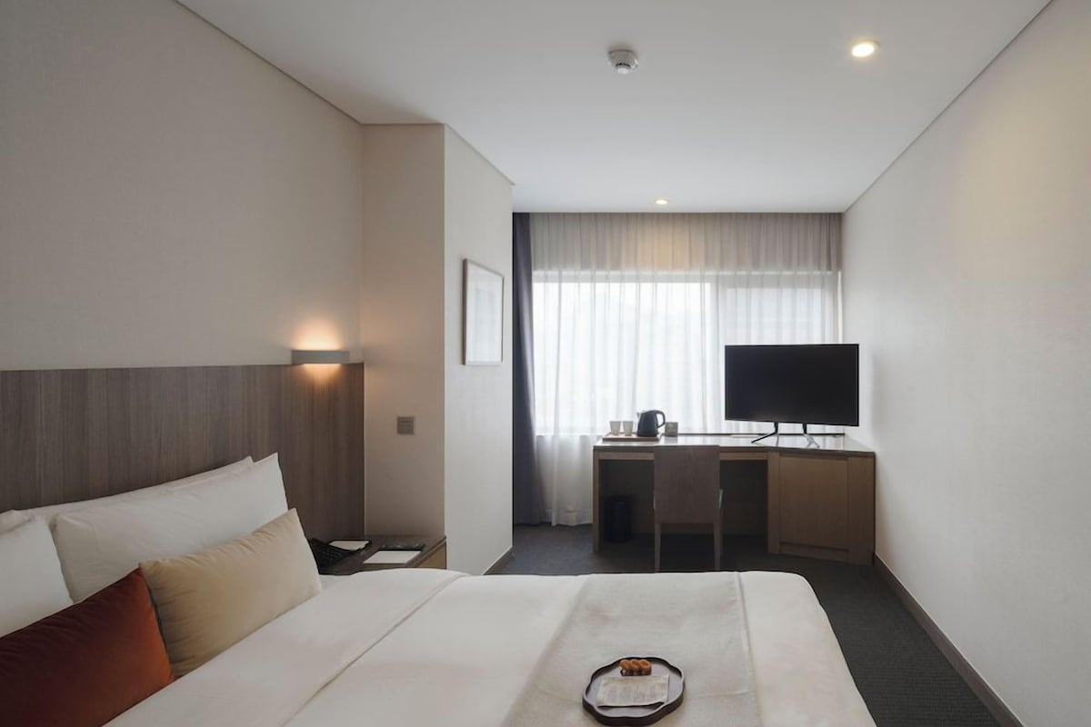 A hotel room with a bed, a desk, a television, and a window with curtains.