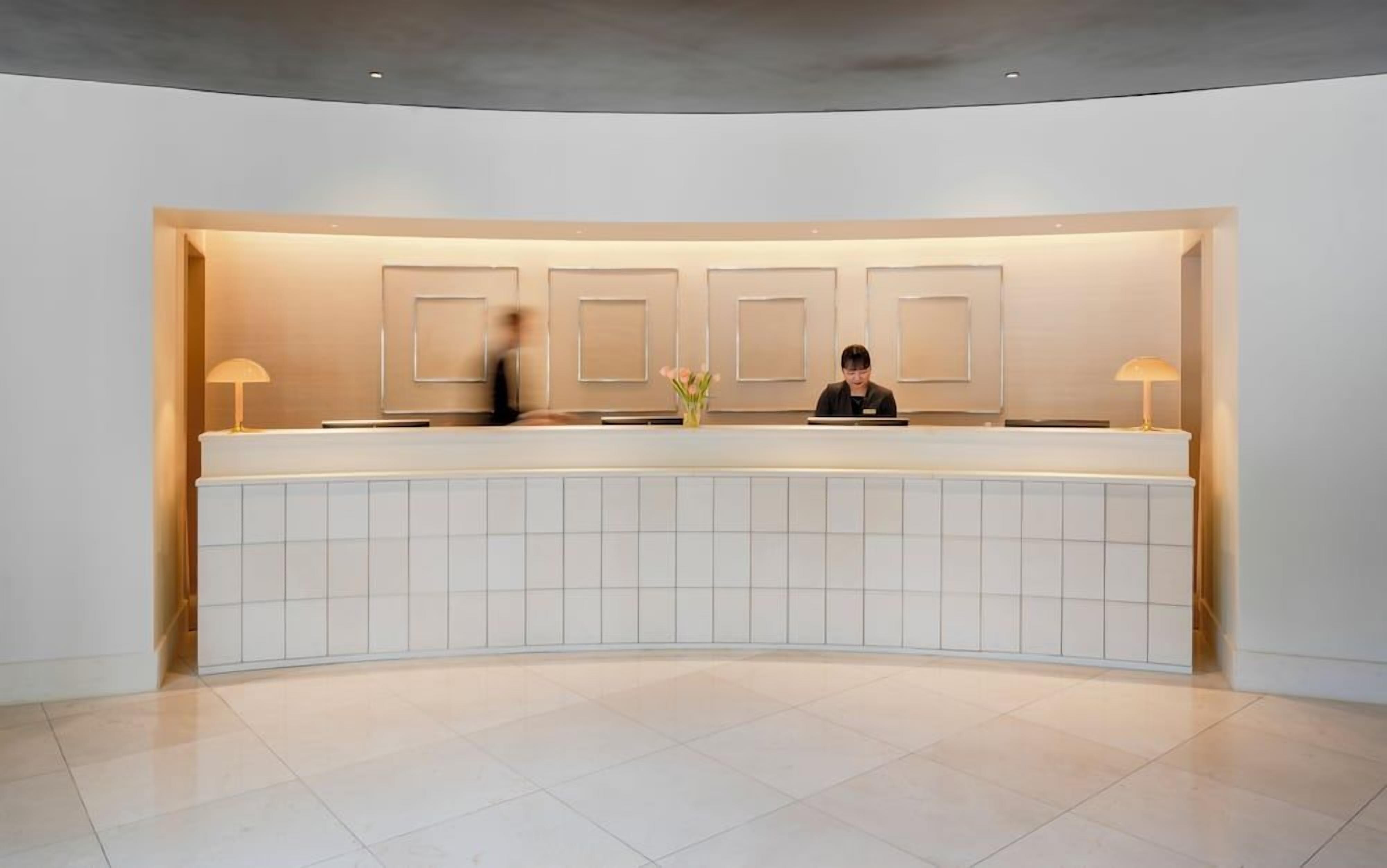 Un mostrador de recepción de diseño moderno, un jarrón con flores y una persona detrás.
