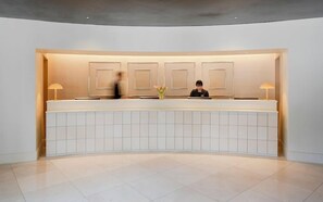A reception desk with a modern design, a vase with flowers, and a person standing behind it. - Amid Hotel Seoul (Seoul)