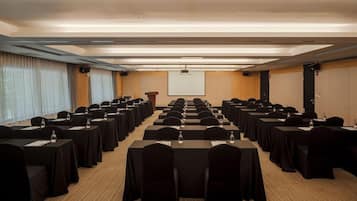 Un salón de conferencias con filas de mesas y sillas, un atril y una pantalla de proyección.