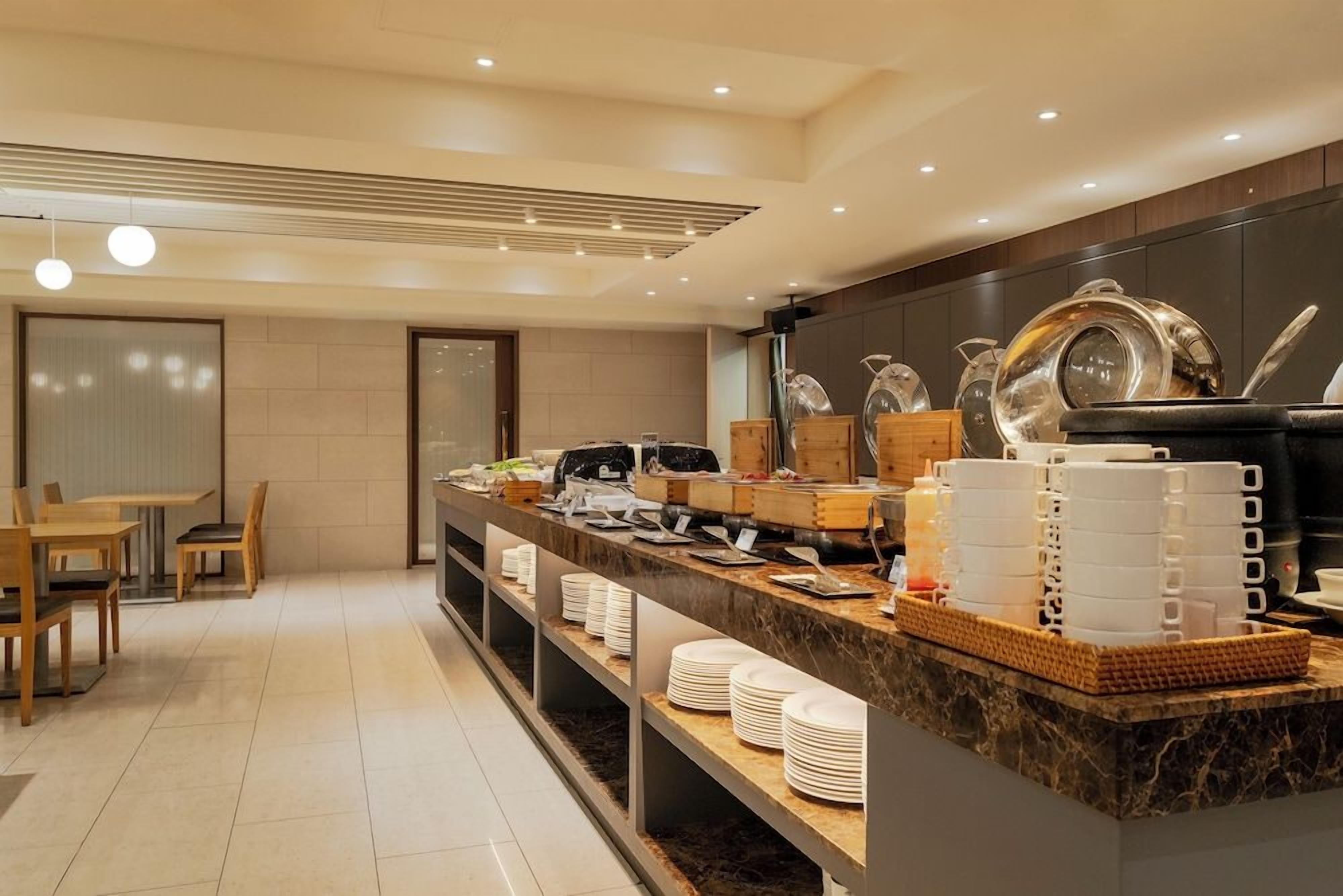 Espaço de café da manhã de um hotel moderno, com balcão de mármore, mesas para refeições e diversas opções de café da manhã.
