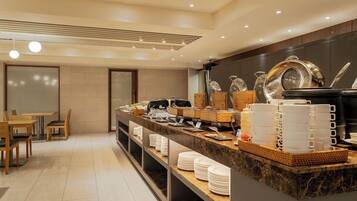 Espaço de café da manhã de um hotel moderno, com balcão de mármore, mesas para refeições e diversas opções de café da manhã.