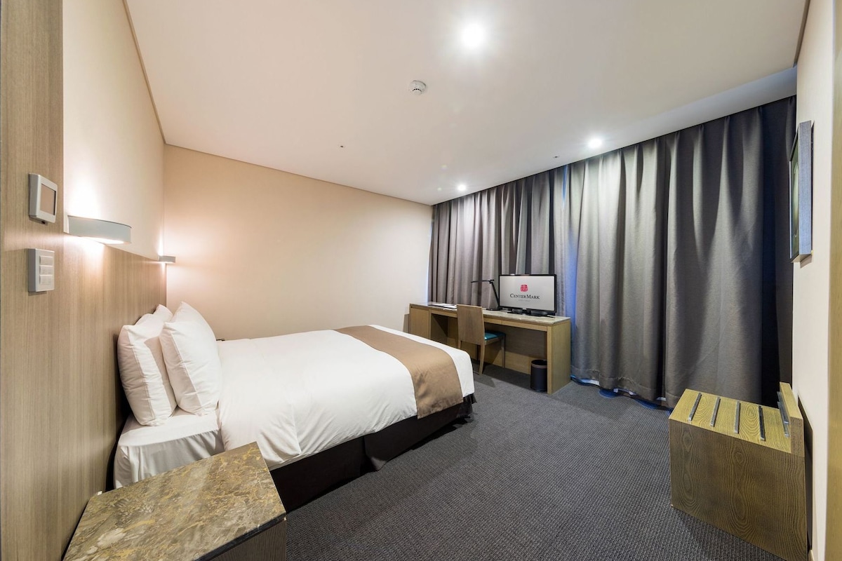 A hotel room with a bed, desk, chair, and curtains.
