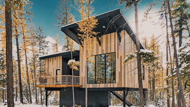 A modern cabin with a wooden exterior, large windows, and a balcony. - Off Grid Stays - Treehouse #4 (Columbia Falls)