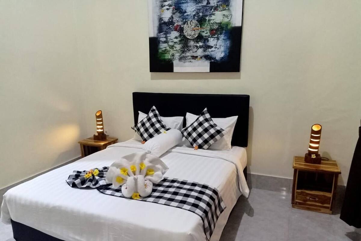 A neatly made bed with a checkered blanket, pillows, and a floral arrangement. There are two bedside tables with lamps.