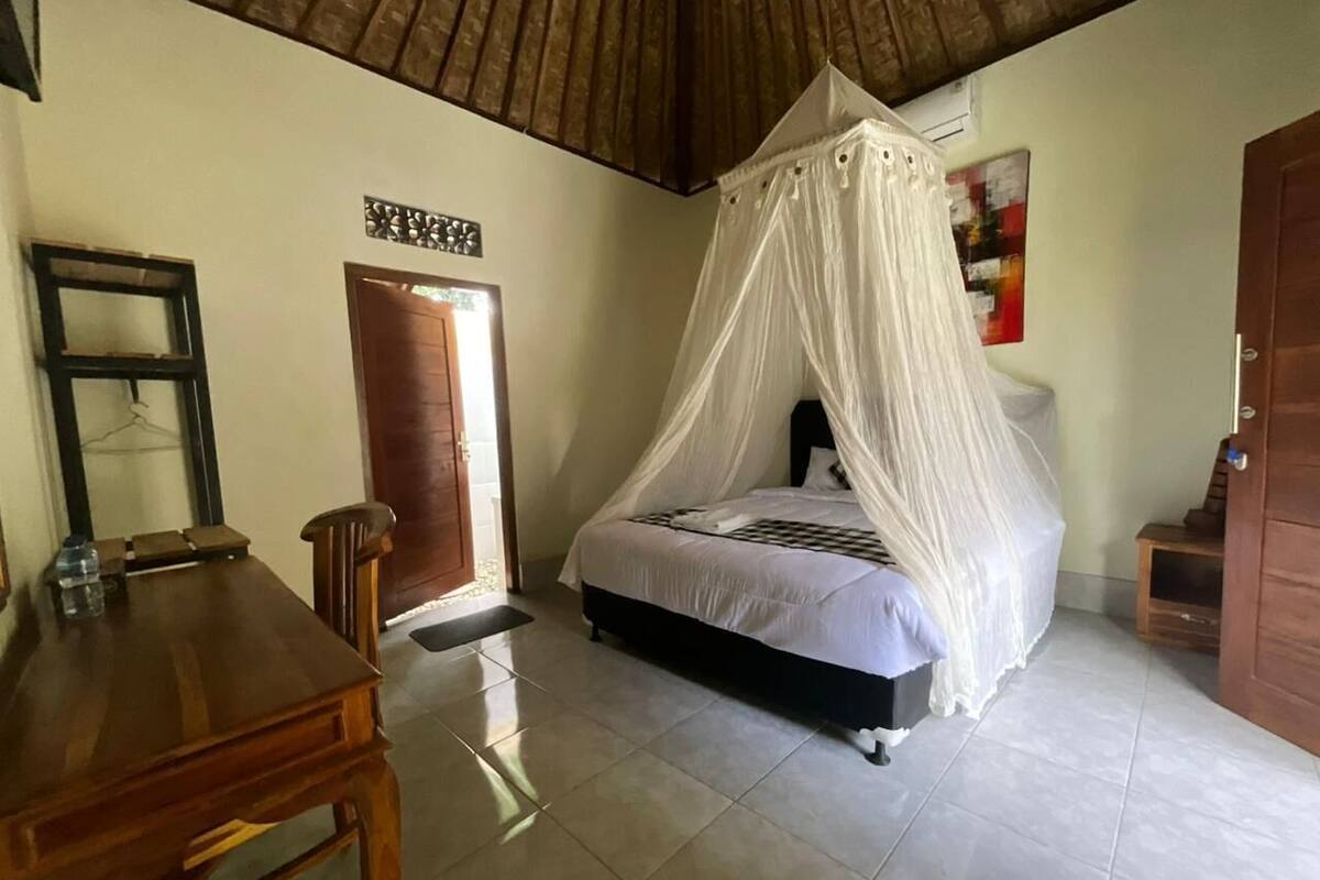 A bedroom with a bed under a canopy, a wooden table, a chair, and a door.